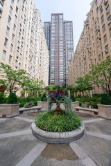 Obraz premium This elegant urban courtyard in New York City features meticulously landscaped gardens surrounded by classic brick buildings. The lush greenery and peaceful setting create a serene retreat amidst the 