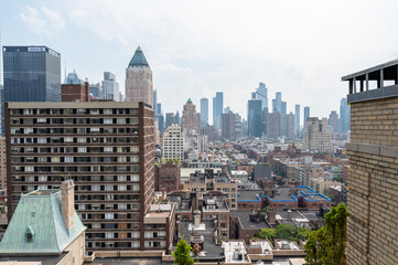 Fototapeta premium This striking New York City photo captures the contrast between towering modern skyscrapers and historic brick buildings, all viewed from a rooftop perspective. The image highlights the architectural 