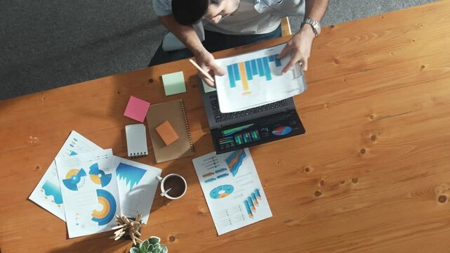 Top aerial view of manager working on laptop while looking at data analysis. Leader compare financial statistic graph while making decision at meeting table with document scatter around. Convocation.