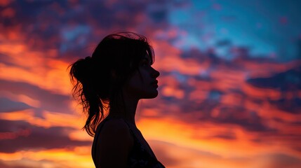 Silhouette of a young woman with her hair tied back standing against a colorful sunset sky reflecting serenity