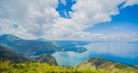 The photo captures the stunning beauty of Lake Toba, with its expansive, shimmering waters surrounded by lush, green hills. The serene lake reflects the clear blue sky and majestic volcanic landscape, © Alvon