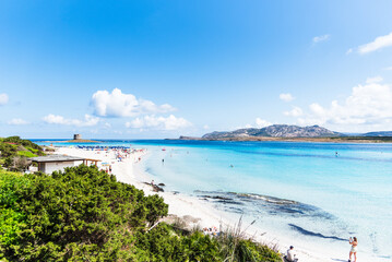 Obraz premium An elevated view reveals the vibrant life of La Pelosa beach, where people dot the shore, blending with the brilliant blue waters of the bay.