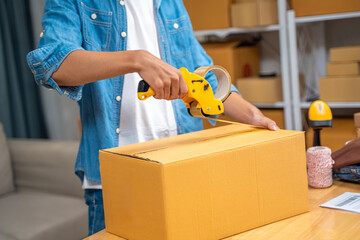 Young online seller man taping  the packing tape on the shipping box before shipping it to his online customer