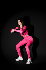 Young woman in sportswear exercising on black background