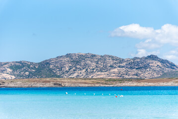 Obraz premium A tranquil blue bay stretches towards the horizon, where Isola Piana rises gently from the sea. Set opposite the famed La Pelosa beach.