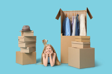 Beautiful young happy woman and wardrobe boxes with clothes lying on blue background