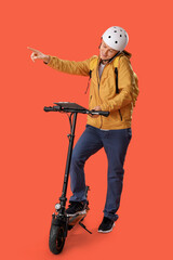 Male courier with clipboard and kick scooter pointing at something while talking by phone on orange background