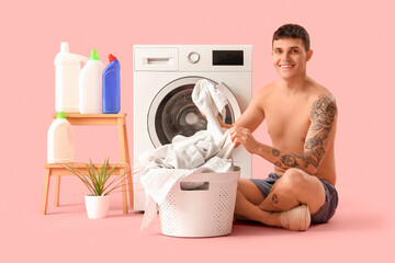 Young man in underpants with basket doing laundry on pink background