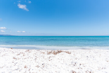 Le Saline beach landscape: turquoise sea meets a distant horizon with faint landforms, under a vast blue sky. A breathtaking view capturing the serene beauty of Sardinia's coastline.