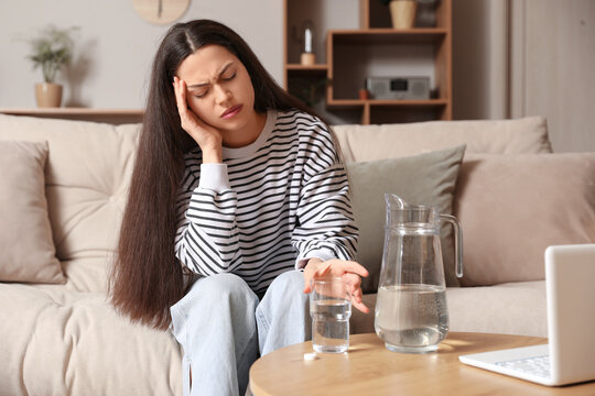 Young woman with glass of water and soluble tablet suffering from headache at home