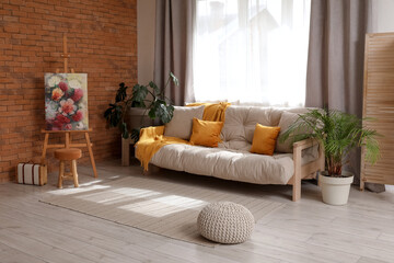 Obraz premium Beautiful picture on easel and cozy sofa in living room