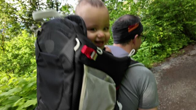 A Father and his Baby Son enjoying a hike together in the forest. The baby is laughing and smiling while in a carrier on his father's back. Chilliwack, British Columbia, Canada.