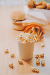 A bucket of popcorn, top-view, warm colors, light brown wooden background, flat lay, daylight macro close-up