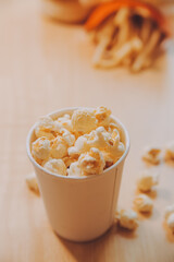 A bucket of popcorn, top-view, warm colors, light brown wooden background, flat lay, daylight macro close-up