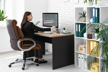 Female office worker using modern computer at workplace in light office