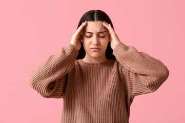 Beautiful young woman suffering from headache on pink background