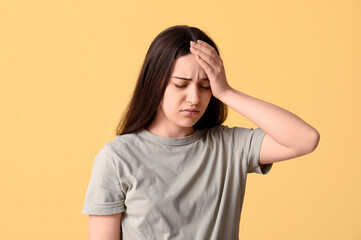 Beautiful young woman suffering from headache on yellow background