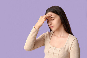 Young woman suffering from headache on lilac background