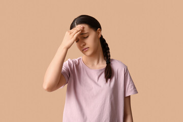 Beautiful young woman suffering from headache on beige background