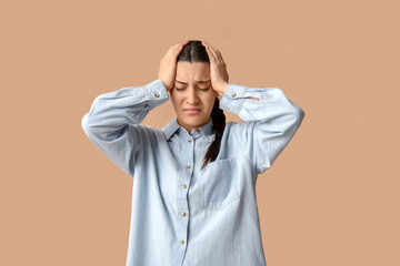 Beautiful young woman suffering from headache on beige background