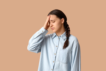 Beautiful young woman suffering from headache on beige background