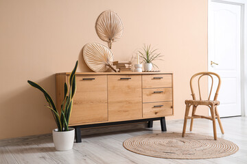 Wooden cabinet with decor and houseplant near beige wall