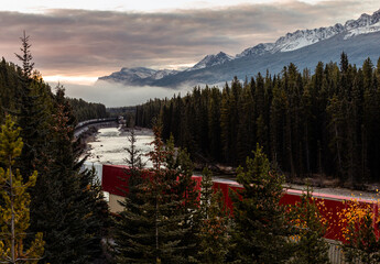 view of a long train with wagons following a curved river on a sunrise with low clouds over the...