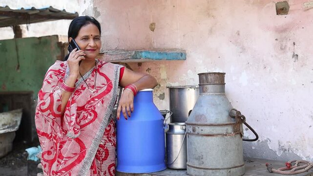 Happy rural indian woman dairy farmer talking on phone after good milk production and profits. Farming industry, Successful business.