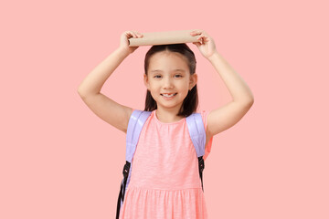 Cute little happy Asian girl with backpack and book on pink background. End of school year