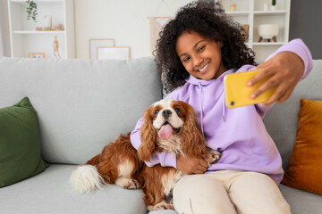 Teen African-American girl taking selfie with cute cavalier King Charles spaniel at home