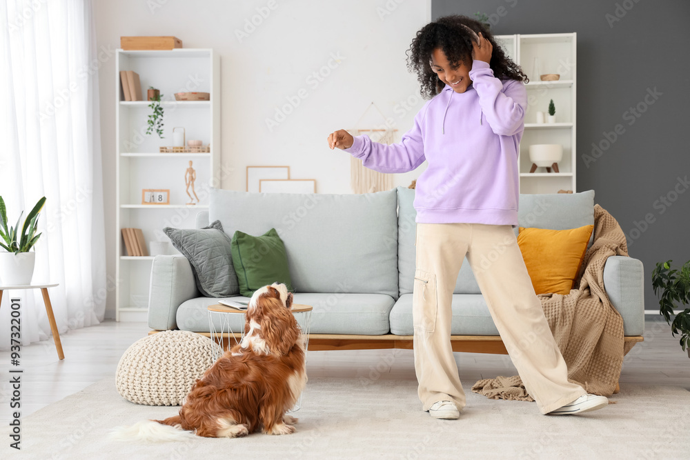 Sticker teen african-american girl in headphones playing with cute cavalier king charles spaniel at home