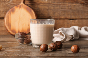 Glass of fresh macadamia milk and bowl with nuts on wooden background