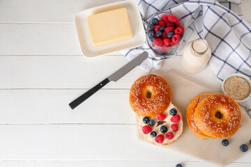 Board of tasty bagels with berries and butter on white wooden background