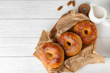 Baking paper with tasty bagels and almond nuts on white wooden background