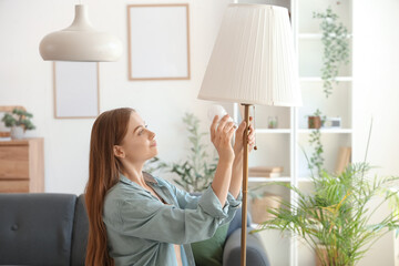 Young woman screwing light bulb into floor lamp at home
