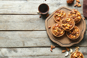 Tasty tarts with nuts and caramel sauce on board against brown wooden background