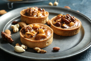 Tasty tarts with nuts and caramel on plates against grunge blue background