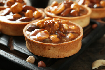 Tasty tarts with different nuts and caramel sauce on wooden board , closeup