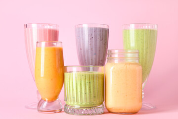 Glasses and mason jar of different fresh smoothie on pink background