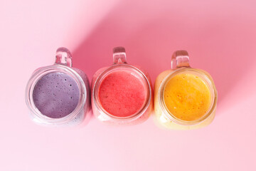 Mason jars of different fresh smoothie on pink background