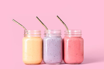 Mason jars of different fresh smoothie on pink background