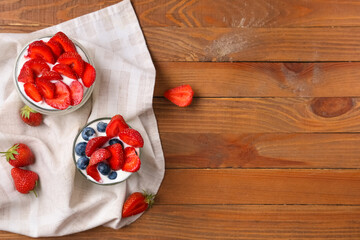 Glass and jar of tasty yogurt with fresh strawberries and blueberries on wooden background