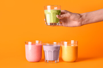 Female hand with glasses of different fresh smoothie on orange background