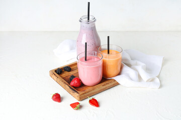 Glasses and bottle of different fresh smoothie with strawberries and blackberries on white...