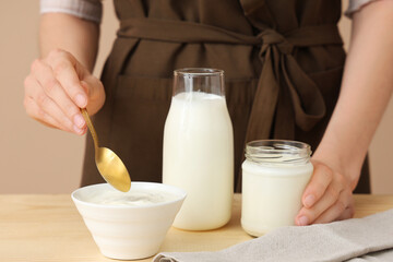 Woman with bowl and jar of tasty yogurt at table on brown background