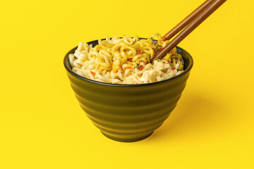 Delicious Instant Ramen Noodles in Black Bowl with Wooden Chopsticks on Vibrant Yellow Background
