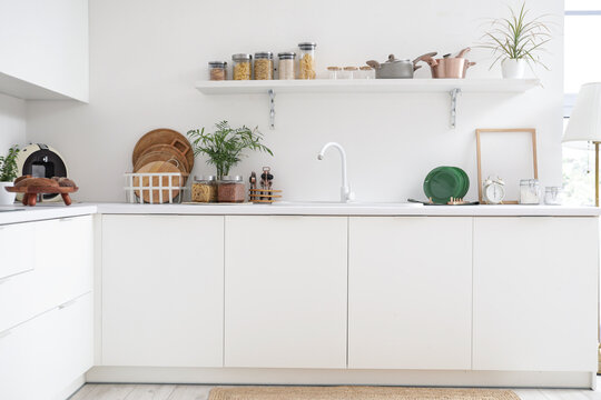 Interior of kitchen with white counters, shelf and utensils