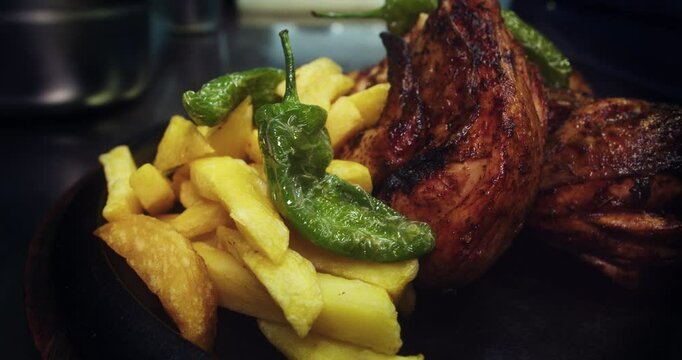 Beautiful slow motion, close-up shot of a plate of charcoal-roasted chicken with fries and padron bell pepper on a wooden plate. 4K