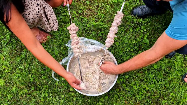 Couple putting fresh delicious meat on skewers for BBQ, top down