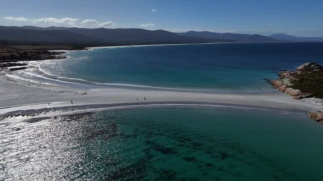 Tourist on sandy beach path visiting Diamond Island during sunny day in Tasmania, Australia. Turquoise ocean water during holidays in summer. Aerial backwards wide shot.